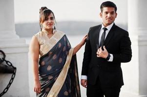 elegante e elegante casal de amigos indianos de mulher de saree e homem de terno posou na margem da marina. foto