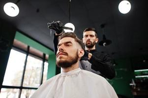 homem barbudo bonito na barbearia, barbeiro no trabalho. foto