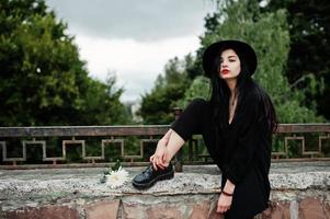 garota sensual toda em preto, lábios vermelhos e chapéu. mulher dramática gótica. foto