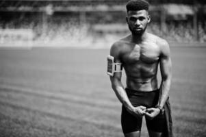 atleta masculino americano africano homem sexy torso nu esporte com capa de braço de esportes em execução para telefone celular, posou na grama verde do estádio de futebol. foto