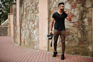 Fotógrafo de homem macho de barba árabe linda e bonita em óculos e camiseta preta com câmera profissional nas mãos. foto