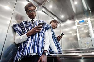 homem africano em roupas tradicionais e óculos com celular no elavator ou elevador moderno. foto