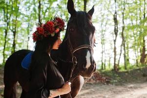 garota mística em grinalda veste em preto com cavalo em madeira. foto