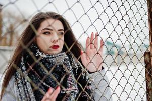 Feche o retrato da menina morena no cachecol contra a gaiola. foto