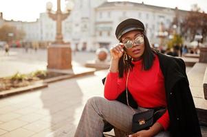 garota de moda afro-americana no casaco e boné de jornaleiro, óculos de sol posou na rua. foto