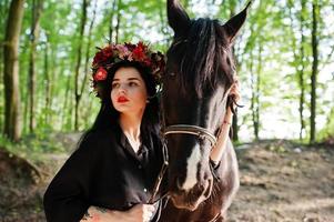 garota mística em grinalda veste em preto com cavalo em madeira. foto