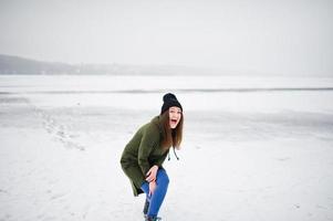 garota engraçada usa moletom verde longo, jeans e chapéu preto, no lago congelado em dia de inverno. foto