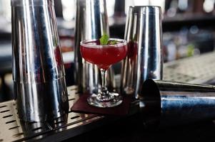coquetel vermelho alcoólico com hortelã na mesa de bar e coqueteleiras. foto