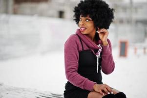 mulher afro-americana de cabelo encaracolado posou em dia de inverno, sentado no banco. foto