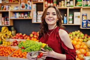 garota de vermelho segurando diferentes vegetais na loja de frutas. foto