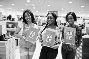 lindas três garotas afro-americanas bem vestidas na loja de sapatos com placas de venda. foto