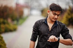 homem indiano de camisa marrom posou ao ar livre e olhando para seus relógios. foto