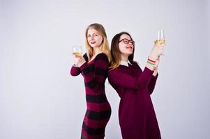 duas amigas atraentes em vestidos roxos bebem vinho espumante ou champanhe no estúdio. foto