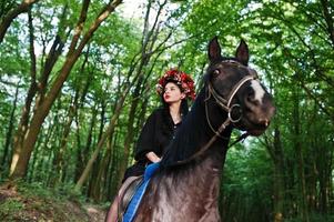 garota mística em grinalda veste de preto a cavalo em madeira. foto