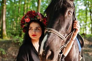 garota mística em grinalda veste em preto com cavalo em madeira. foto