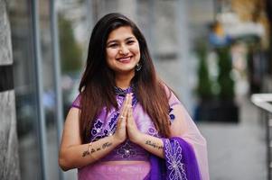 garota hindu indiana no tradicional saree violeta posou na rua e mostra o sinal de mãos tatuadas namastê. foto