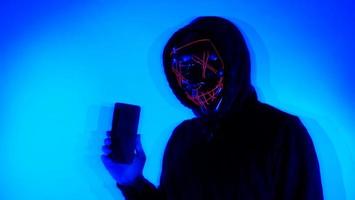 hacker anônimo e máscara facial com smartphone na mão. foto