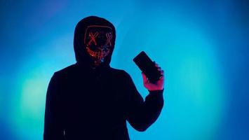 hacker anônimo e máscara facial com smartphone na mão. foto
