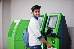 jovem asiático colocou seu cartão de crédito para retirar dinheiro de um caixa eletrônico verde. foto