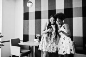 duas namoradas africanas negras felizes em vestidos de verão olhando no celular no café. foto