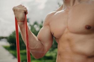 homem forte irreconhecível tem treino com banda de resistência, fica mais forte a cada dia, mostra corpo bem construído, poses ao ar livre. esporte, musculação e conceito de estilo de vida saudável. atleta sem rosto foto