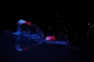 atleta de triatlo real nadando na noite escura foto