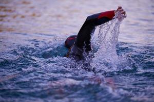 atleta de triatlo nadando no lago ao nascer do sol vestindo roupa de mergulho foto