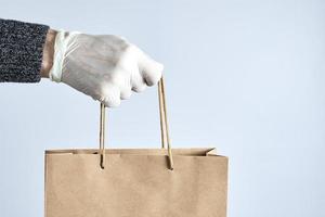 mão em luvas de borracha branca segura um saco de papel. conceito de compras seguras. entrega de alimentos durante a quarentena da pandemia de coronavírus. foto