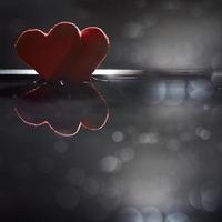 dois corações vermelhos são refletidos na água em um fundo escuro com um bokeh. foto com espaço de cópia.
