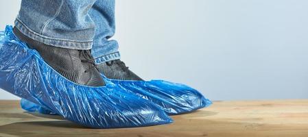 homem com capas de sapato azul usado sobre sapatos clássicos em fundo cinza, closeup. luta contra a infecção. foto