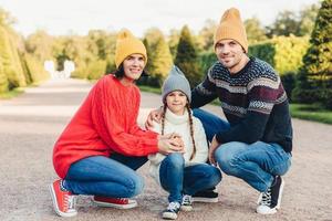 família amigável usa roupas de malha, caminha juntos, admira o esplêndido clima de outono. pais jovens afetuosos e sua filhinha brincam juntos ao ar livre. conceito de relacionamento foto