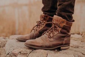 imagem do homem em calças e botas de couro velho marrom fica em pedras contra o fundo desfocado. sapatos surrados. venda de sapatos. inverno chegando foto