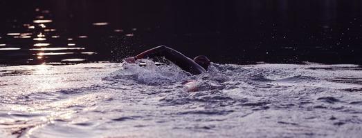 atleta de triatlo nadando no lago ao nascer do sol vestindo roupa de mergulho foto