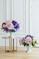 vasos altos com lindas flores artificiais na mesa e no chão no espaçoso salão de banquetes. arranjo floral para casamento. rosas delicadas. conceito de decoração foto