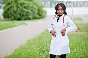jovem médica afro-americana de jaleco branco com um estetoscópio posou ao ar livre. foto