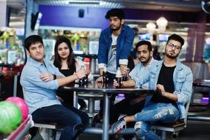grupo de cinco povos do sul da Ásia descansando e se divertindo no clube de boliche, sentado na mesa e bebendo refrigerantes em garrafas de vidro. foto