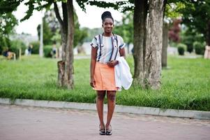 jovem médica afro-americana segura jaleco branco por lado com um estetoscópio posado ao ar livre. foto