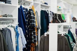 conjunto de roupas coloridas femininas nas prateleiras com sapatos na loja de roupas nova boutique moderna. foto