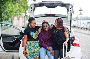 três amigos afro-americanos sentam-se no porta-malas do carro. foto