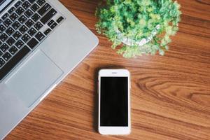 foto plana leiga de mesa de escritório com laptop, smartphone e planta com fundo de madeira