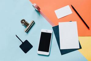 mesa de trabalho criativa de estilo plano leigo com smartphone, envelope em branco, óculos de sol e fita adesiva em fundo colorido moderno foto