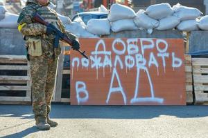perto da inscrição bem-vindo ao inferno um defensor da defesa territorial de kyiv em um posto de controle com uma metralhadora pronta em um dia ensolarado de primavera fica 28.02.22. ktiv. Ucrânia.