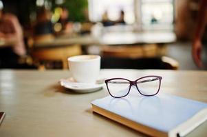 feche a foto do notebook com óculos contra a xícara de café na mesa de café. conceito de óculos.