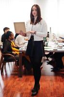 rosto de mulher de negócios europeu bonito, segurando o laptop no fundo da reunião de equipe multirracial de pessoas de negócios, sentado na mesa do escritório. foto