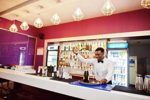 barman americano africano no bar segurando champanhe com copos na bandeja. foto
