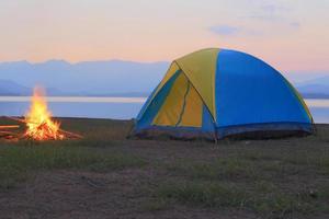 tenda e fogueira ao pôr do sol, ao lado do lago foto