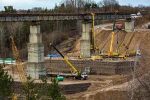 construção ou reconstrução de ponte de concreto rodoviário sobre um rio largo. máquinas de construção, caminhões e guindastes trabalham foto