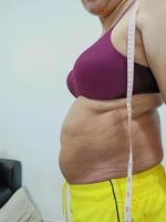 vista lateral. mulher asiática gorda surrada em pé mostrando sua barriga foto