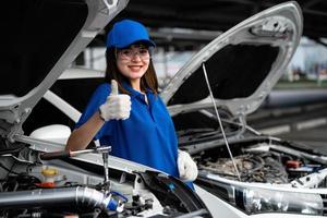 centro de serviço de reparação de automóveis, um mecânico feminino feliz ao lado do carro. mecânico de carro de mulher asiática vestindo camisa aquarela na garagem. mecânico de mulher feliz no centro de serviço de reparação de automóveis. foto