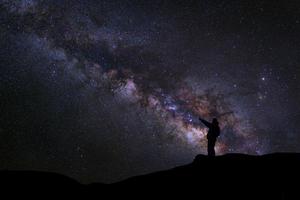 um homem está de pé ao lado da via láctea apontando para uma estrela brilhante, fotografia de longa exposição, com grãos foto
